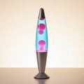 A glowing lava-style night lamp with a silver base and a pink-to-blue gradient chamber sits on a wooden table at dusk. A coffee cup, books, and a balcony railing are visible in the background, with the text 'MAGMA MOTION NIGHT LAMP' overlaid in the upper left.